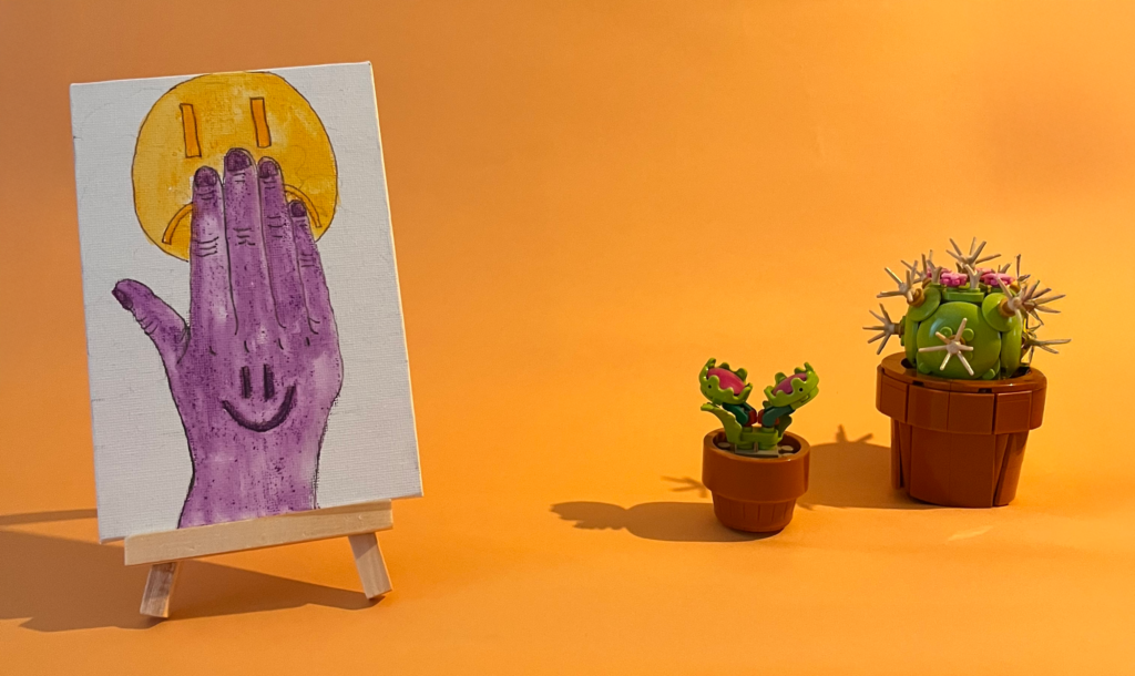 Photographie de l'oeuvre unique originale : une main avec un smiley content dessiné dessus cache un smiley triste à l'arrière
