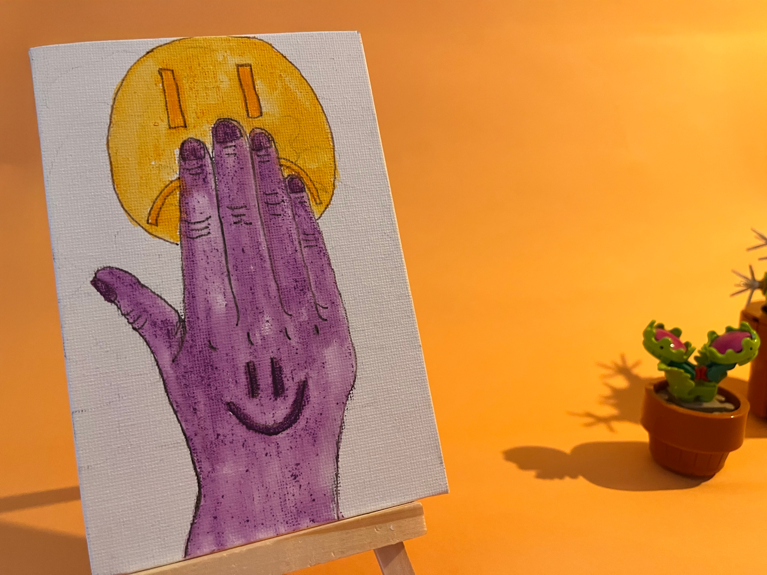 Photographie de l'oeuvre unique originale : une main avec un smiley content dessiné dessus cache un smiley triste à l'arrière